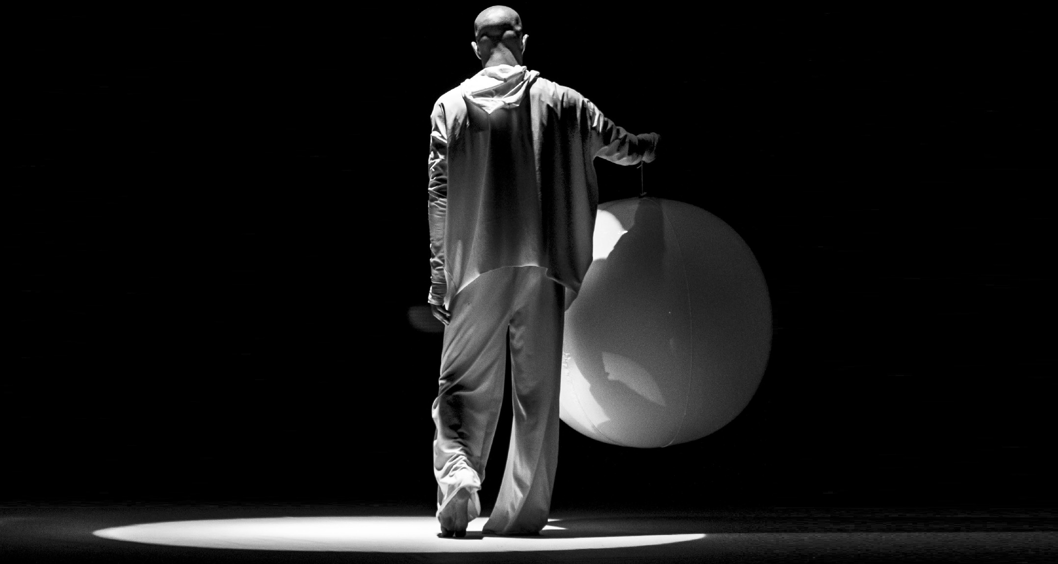 Fotografía en blanco y negro de un actor de teatro botando una pelota gigante