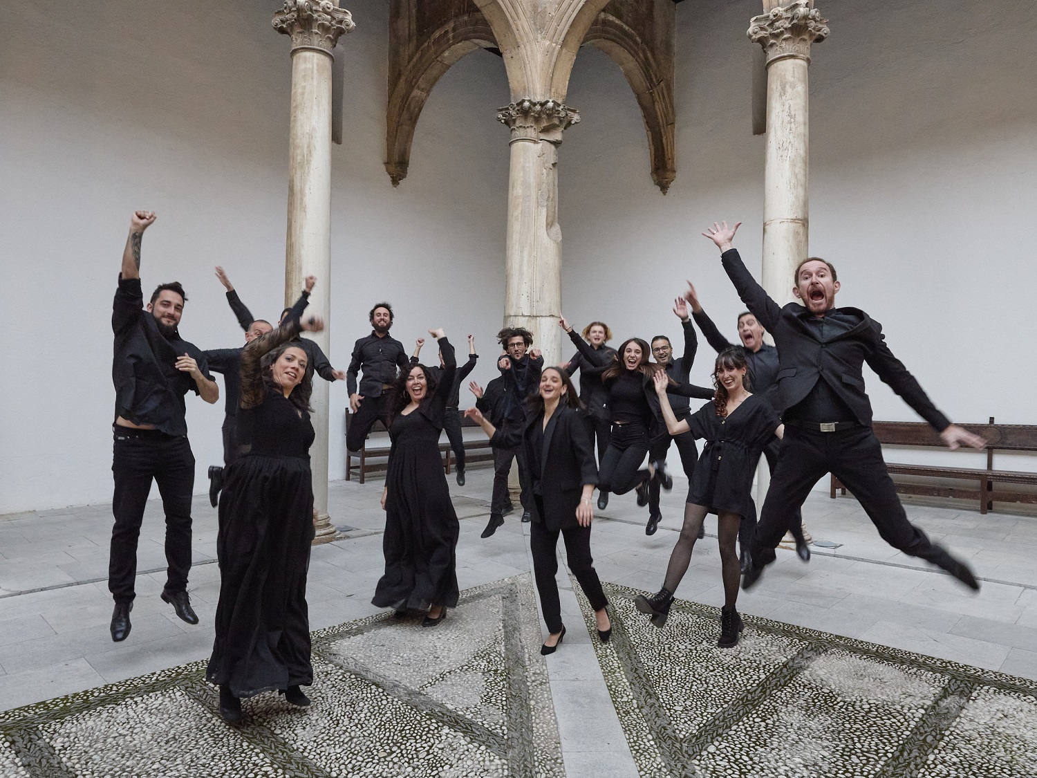 Fotografía de los integrantes del Coro de la UGR saltando de alegría en un patio del Hospital Real de Granada