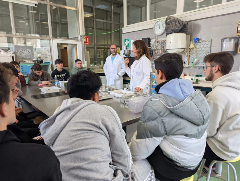 Grupo de estudiantes prestando atención a la explicación de dos investigadores en un laboratorio